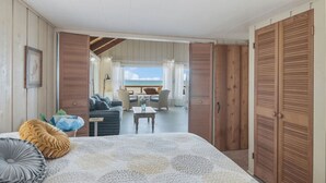 Une chambre avec un lit, donnant sur un balcon aménagé avec des sièges, et dotée de portes en bois.