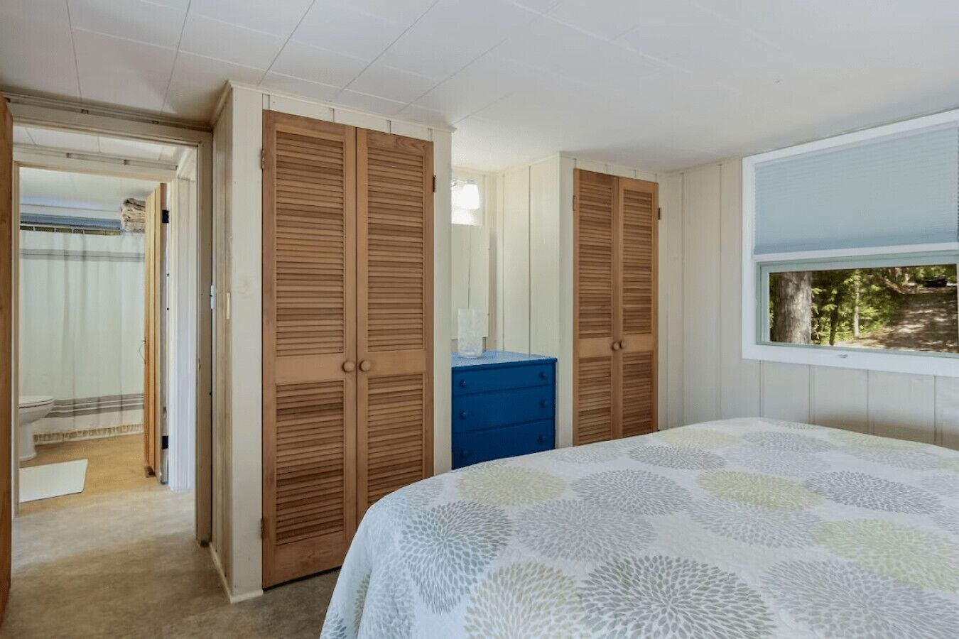 Ein Schlafzimmer mit zwei Holzschränken, einer blauen Kommode und einem Bett mit einem gemusterten Bettbezug.