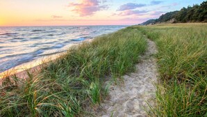 Un sentier côtier, bordé d’herbe et de sable, qui mène à la mer, sous un ciel embrasé par le coucher du soleil.