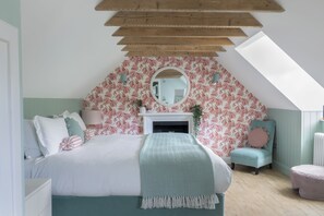 A bedroom with a sloped ceiling, a bed with a herringbone-patterned throw, a round mirror, and a fireplace.