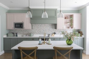 A kitchen with a central island, two wooden chairs, pendant lights, and a variety of kitchen appliances and decor.