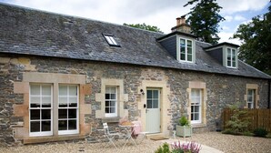 A stone house with a gravel driveway, a small garden, and a wooden fence. - Stables Cottage, Kailzie - sleeping 2 guests in one bedroom (Peebles)