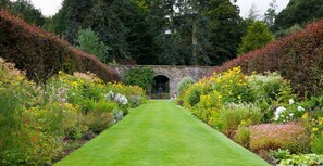 A garden pathway leading to a stone archway surrounded by diverse flowering plants and trees. - Stables Cottage, Kailzie - sleeping 2 guests in one bedroom (Peebles)