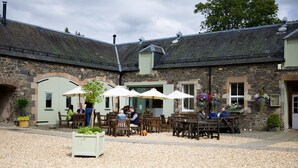 A stone building with outdoor seating and umbrellas. - Stables Cottage, Kailzie - sleeping 2 guests in one bedroom (Peebles)