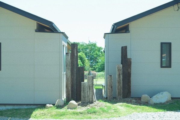 A building with two separate sections, each with a door and a window. There are wooden posts and rocks in front of the building.