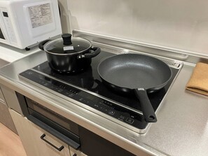 Een koelkast, een magnetron, een kookplaat, kookgerei, borden en bestek