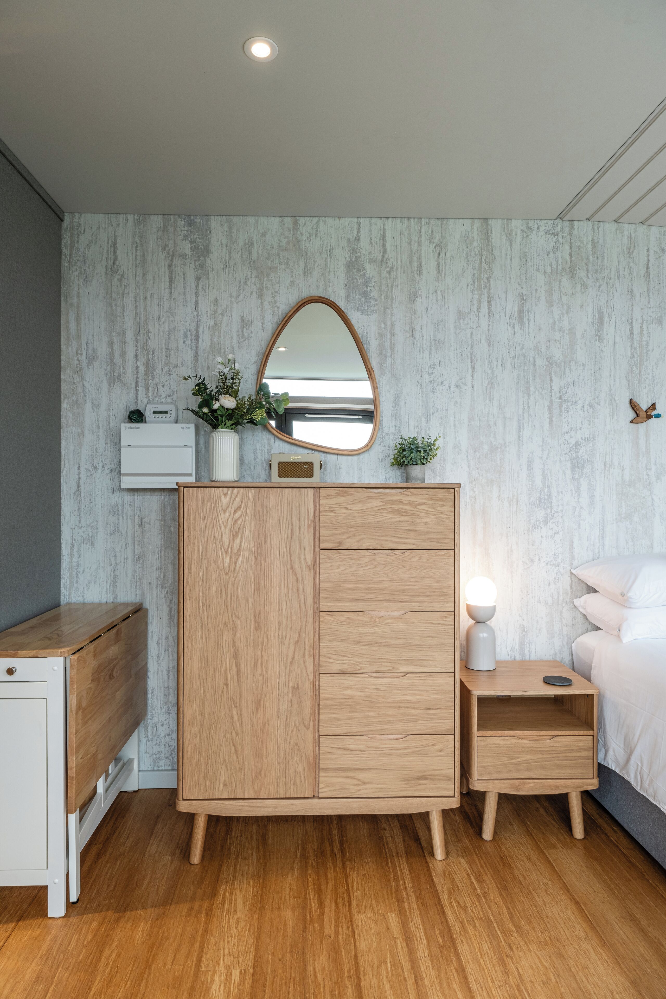 A bedroom with a wooden wardrobe, bedside table, and a bed.