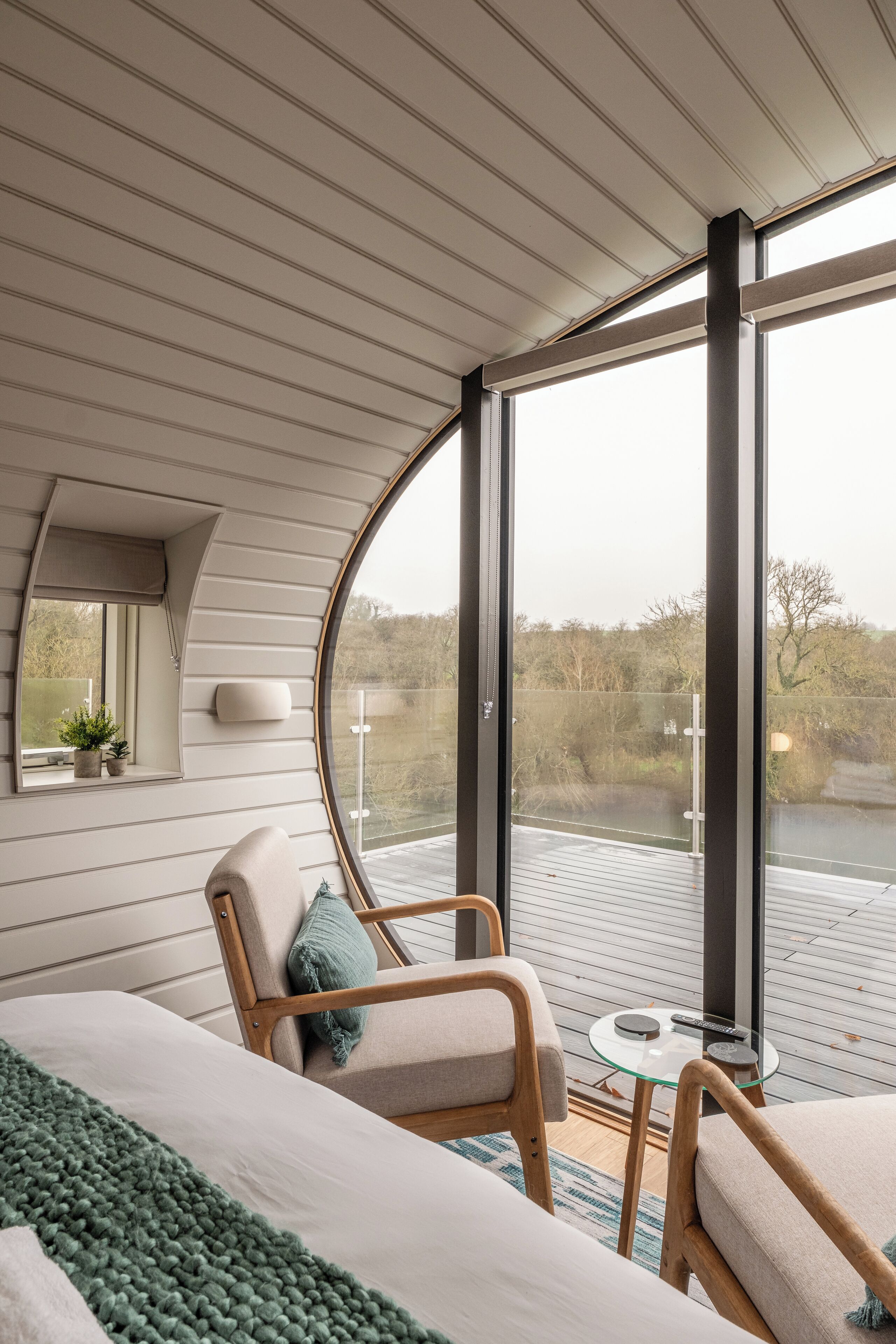 Ein modernes Zimmer mit gewölbter Decke, großen Fenstern, einem Bett, zwei Stühlen, einem kleinen Tisch und Blick ins Freie.