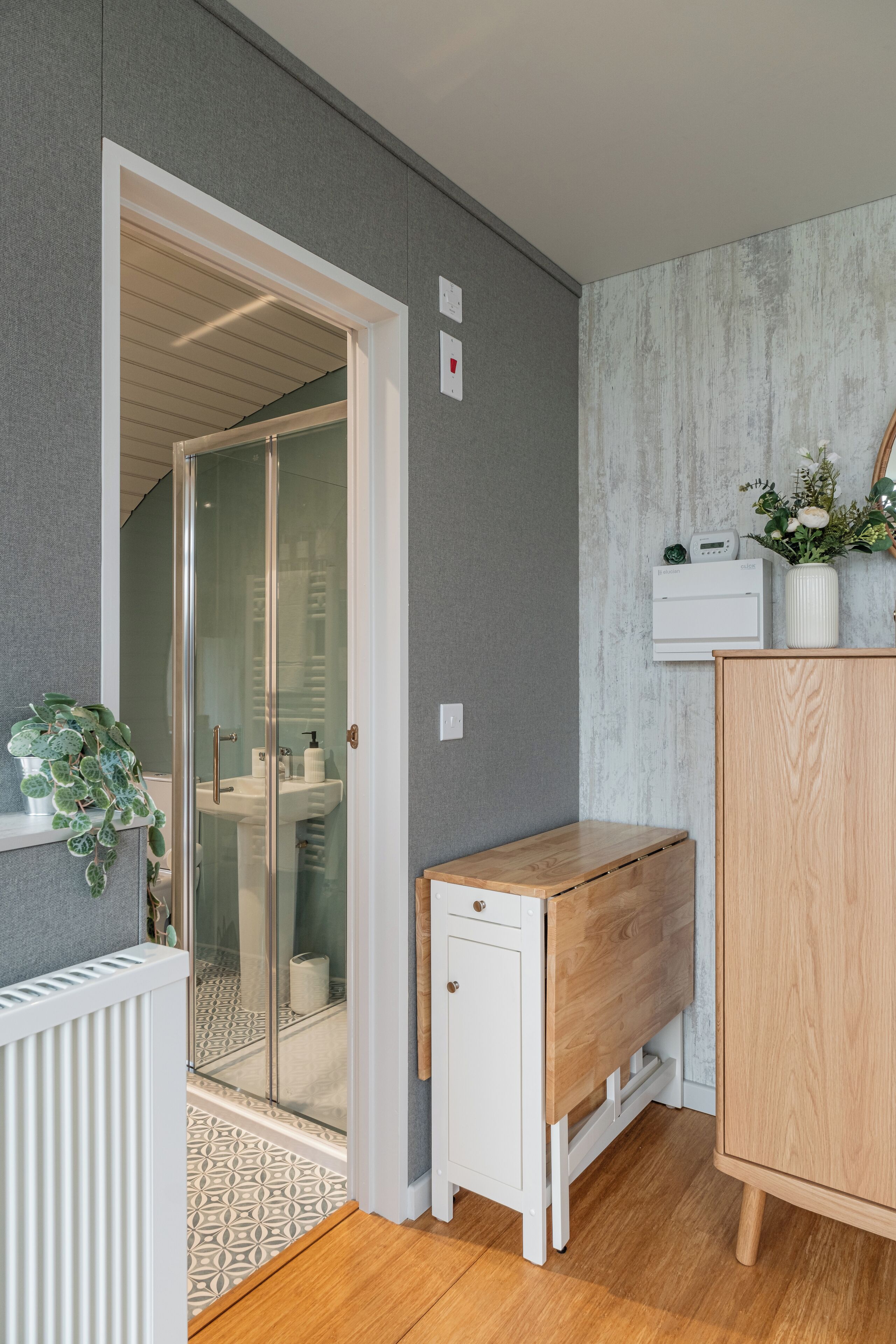 A modern bathroom with a glass shower enclosure, a wooden bench, and a white radiator.