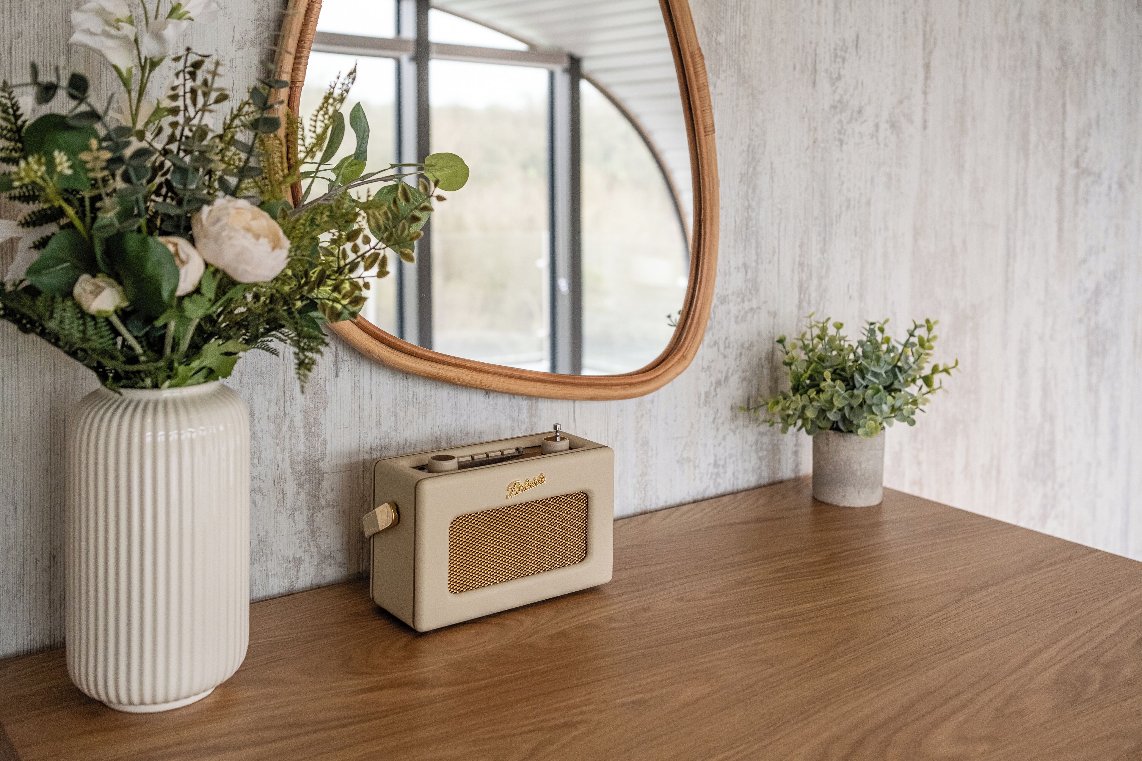 A vintage radio, a large vase with flowers, and a smaller potted plant on a wooden surface.