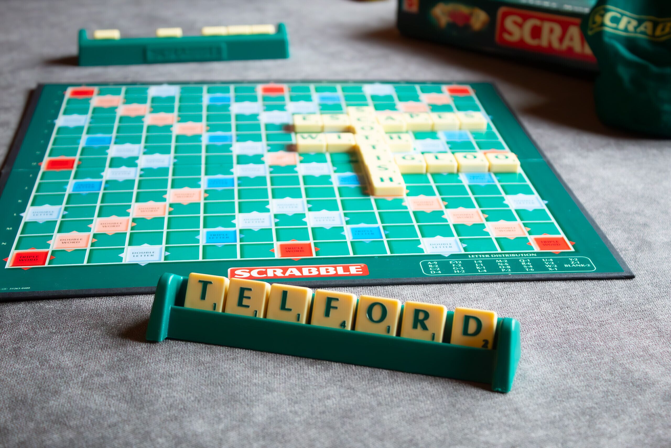 A Scrabble game board with tiles spelling "TELFORD" and a Scrabble box in the background.