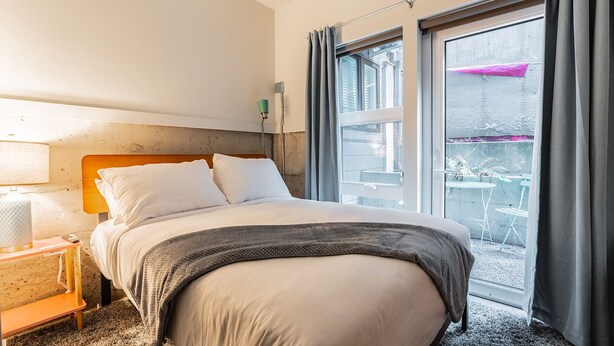 Een hotelkamer met een bed, nachtkastje, lamp en raam met gordijnen.