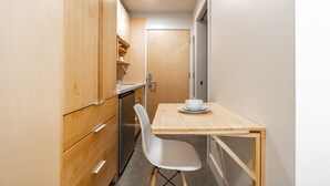 Een compacte keuken met houten kastjes, een witte stoel en een kleine tafel met een kom.