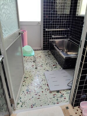A bathroom with a tiled floor, a bathtub, a toilet, and a shower area.
