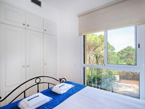 Un dormitorio con cama, ventana con vista a árboles y un armario blanco.