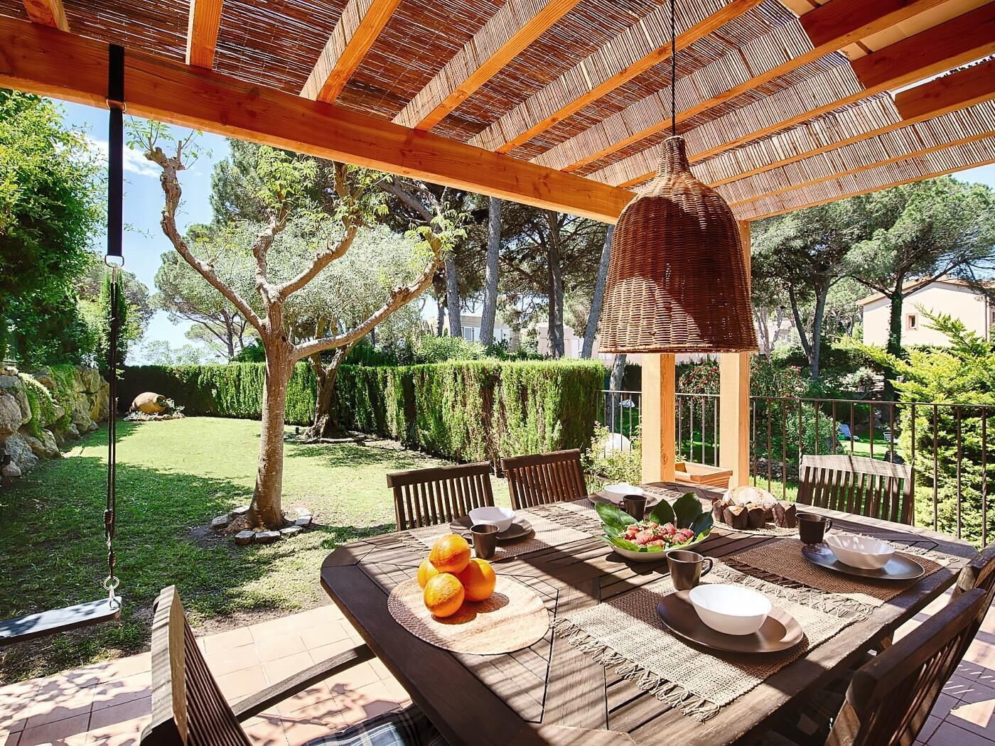 An outdoor dining area with a wooden table, chairs, and a hanging light fixture.