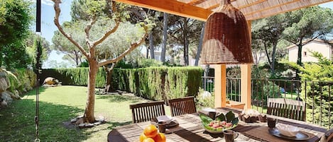 An outdoor dining area with a wooden table, chairs, and a hanging light fixture.