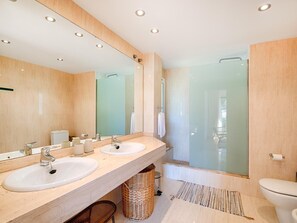 Un baño moderno con dos lavamanos, un espejo grande, cabina de ducha y un inodoro.