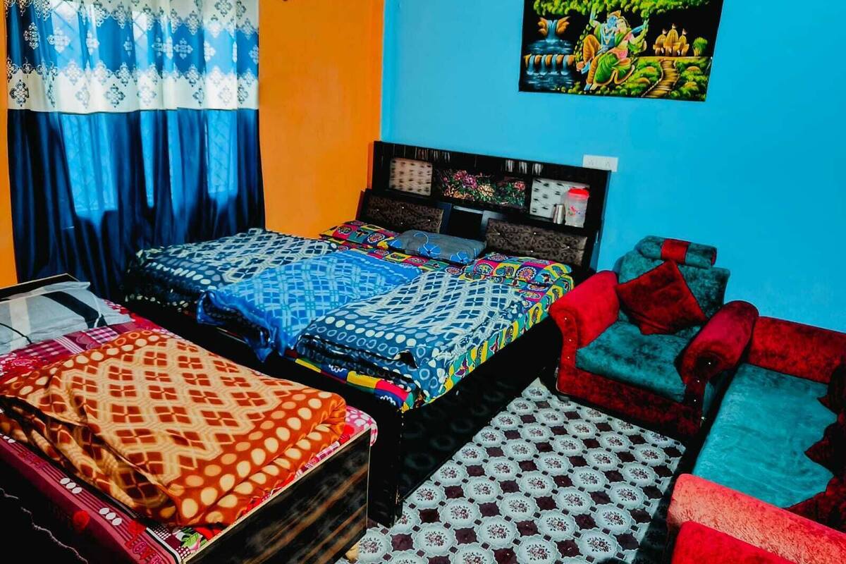 Une chambre avec deux lits, un canapé rouge et un mur orné d’un tableau coloré.