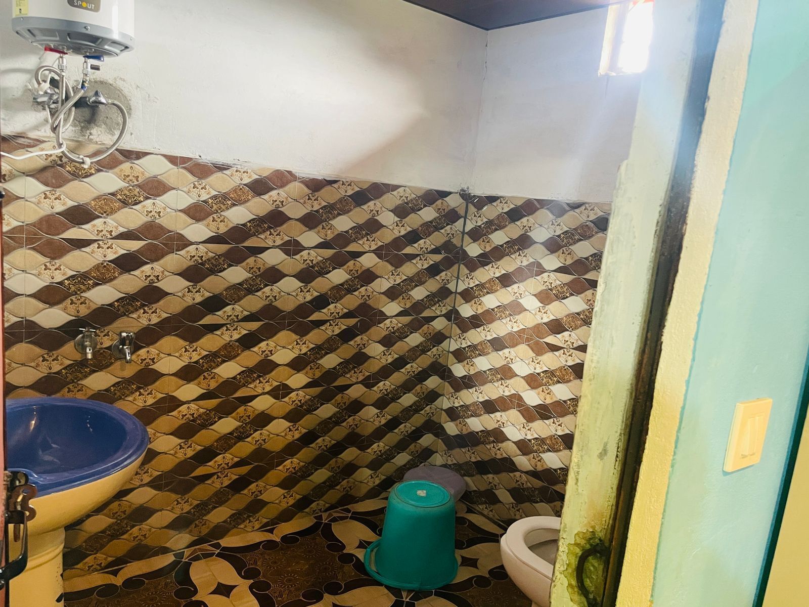 A bathroom with a patterned tile wall, a blue sink, a white toilet, and a green trash bin.