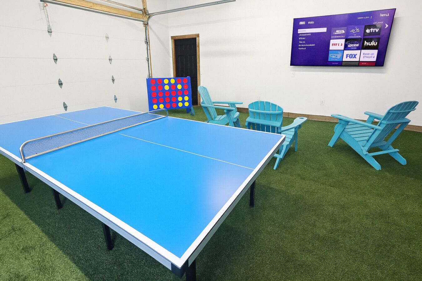 Une table de ping-pong avec quatre chaises, un téléviseur diffusant différentes chaînes et une porte à l’arrière-plan.
