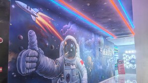 A space-themed mural with an astronaut giving a thumbs-up, a rocket, and planets. - Meihao Exquisite Hotel (Guangzhou)