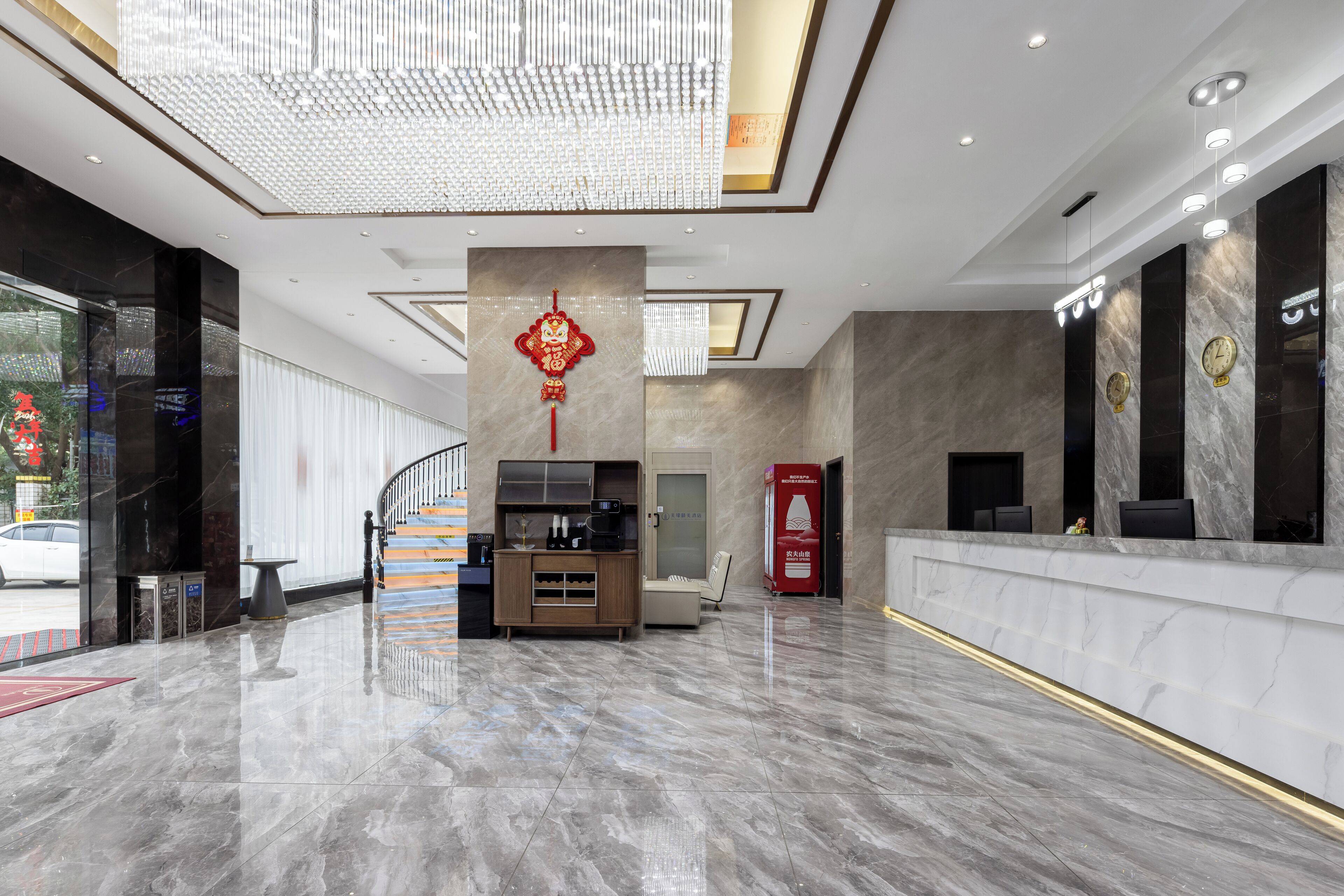 A modern hotel lobby with a marble floor, a reception desk, a staircase, and a decorative red hanging ornament.