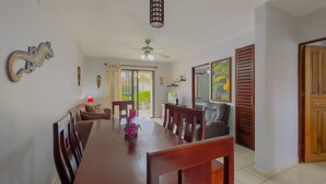 A dining area with a wooden table, chairs, a ceiling fan, and a view through a glass door to the outdoors.