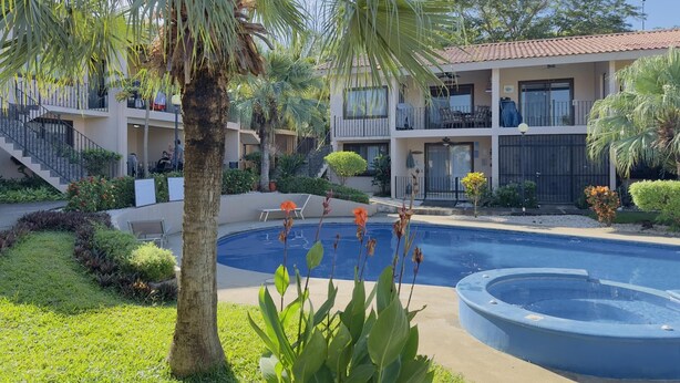 A pool area with a palm tree, a building with balconies, and a staircase.