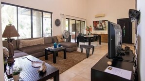 A living room with a sofa, coffee table, and TV. There is a dining area with chairs and a table.