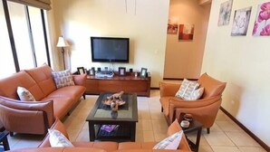 Un salón con dos sofás de cuero marrón, una mesa de centro, un televisor y una mesita auxiliar.