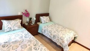 Un dormitorio con dos camas individuales, cada una con una colcha estampada y almohadas a juego. Hay una mesita de noche con una lámpara y un florero con flores entre las camas.