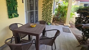 A patio area with a table and chairs, a metal gate, a green wall with plants, and a view of the surrounding garden. - Cormoran A2 2 bed 2 Bath Condo In las Palmas (Playas del Coco)
