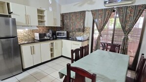A compact kitchen with a refrigerator, microwave, and sink. There is a dining table with chairs and a window with curtains. - Cormoran A2 2 bed 2 Bath Condo In las Palmas (Playas del Coco)