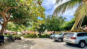 A parking area with several cars and motorcycles, surrounded by lush greenery and palm trees. - Cormoran A2 2 bed 2 Bath Condo In las Palmas (Playas del Coco)