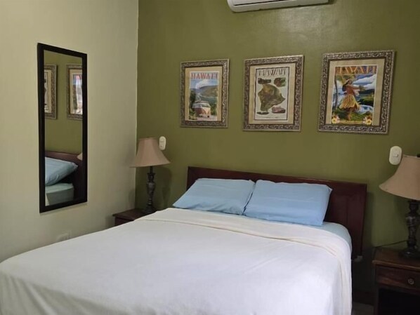 Une chambre d’hôtel avec un lit, deux tables de chevet, un miroir et trois tableaux encadrés accrochés au mur.