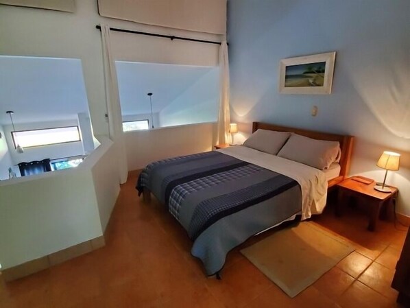 A bedroom with a bed, a nightstand, a window, and a view of a balcony.