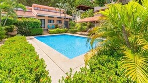 Una piscina rodeada de abundante vegetación y un edificio con techo de tejas.