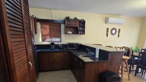 A kitchen with wooden cabinets, a microwave, a sink, and a dining area with chairs. - Vista Hermosa D2 2 bed 2 bath Spacious & Fully Equipped Condo (Playa Hermosa)