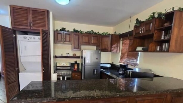 A kitchen with wooden cabinets, a granite countertop, a refrigerator, a stove, and two wicker chairs. - Vista Hermosa D2 2 bed 2 bath Spacious & Fully Equipped Condo (Playa Hermosa)