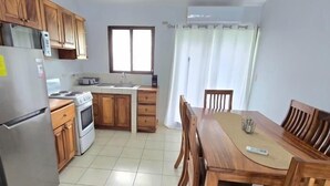 A kitchen with wooden cabinets, a refrigerator, a stove, and a dining table with chairs. - Green Life #3 | Perfect Beachside Living (Playas del Coco)