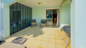 A sunlit patio with a tiled floor, two chairs, a grill, and a sliding glass door leading to an indoor area. - Green Life #3 | Perfect Beachside Living (Playas del Coco)