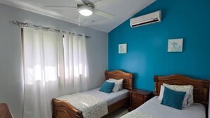 A bedroom with two wooden beds, a ceiling fan, an air conditioning unit, and a window with sheer curtains. - Green Life #3 | Perfect Beachside Living (Playas del Coco)