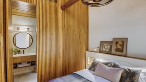 A bedroom with a wooden slatted wall, a round mirror, a bedside table with a lamp, and a bed with multiple pillows. - 8 Leyn Baan Street (Galle)