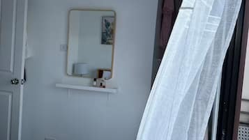 A bedroom with a bed, a bedside table, a mirror, and a window with a curtain.