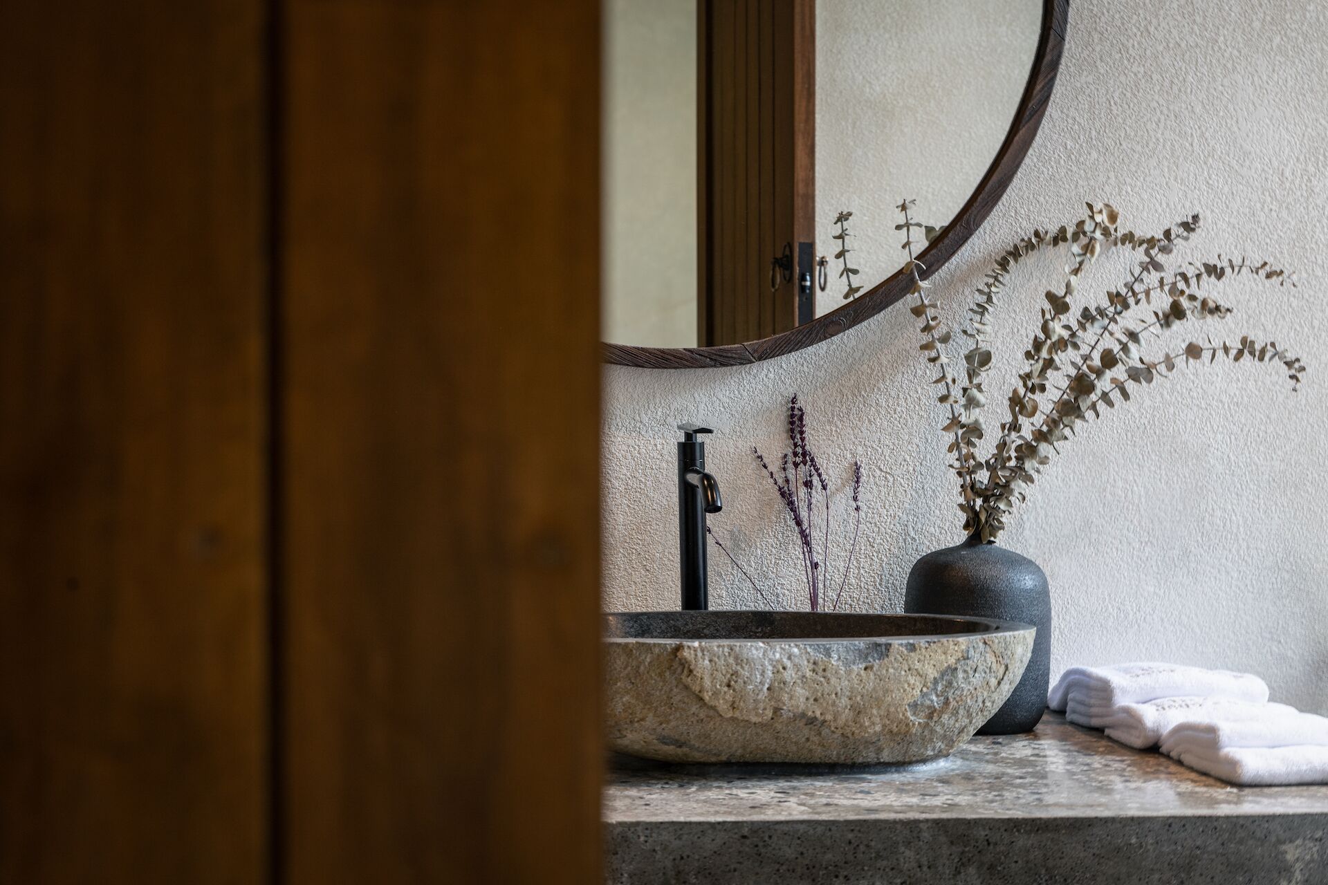 A bathroom with a stone sink, a wooden door, and a mirror with a wooden frame.