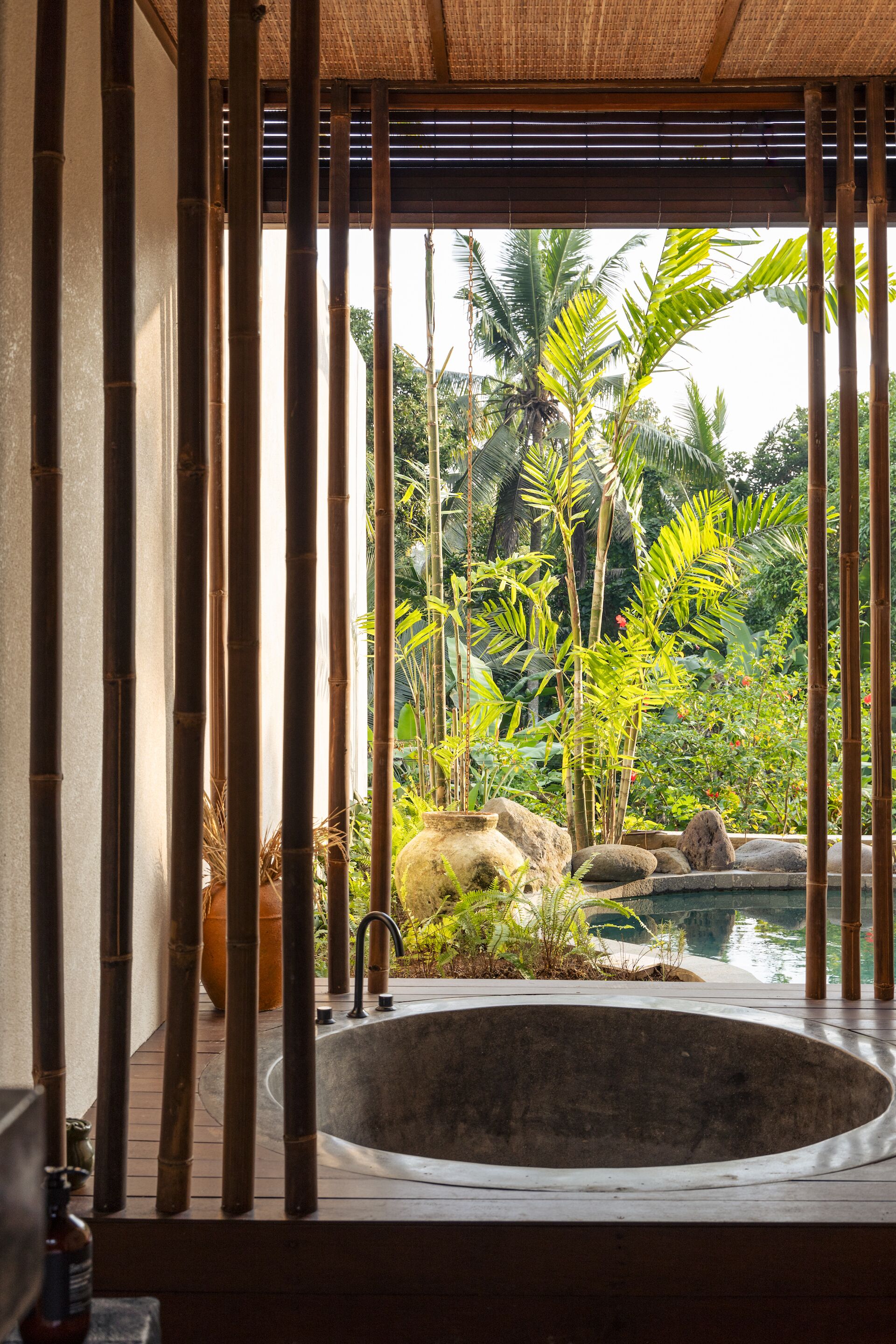 Een wellnessruimte met een grote ronde jacuzzi, bamboepalen en tropische planten.