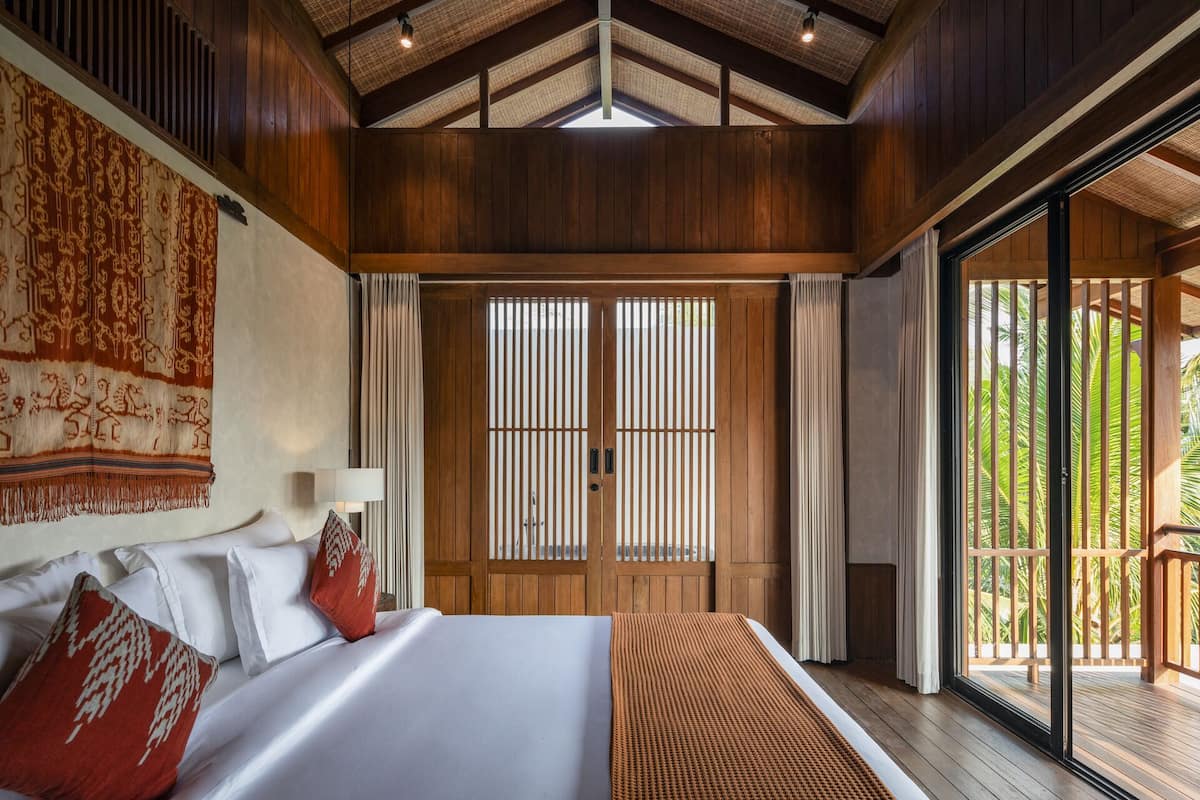 A spacious bedroom with a large bed, a wooden ceiling, and a sliding glass door leading to a balcony.