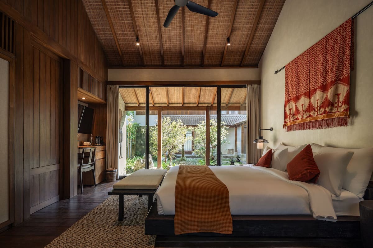 A spacious bedroom with a large bed, a ceiling fan, and a view of a traditional courtyard.
