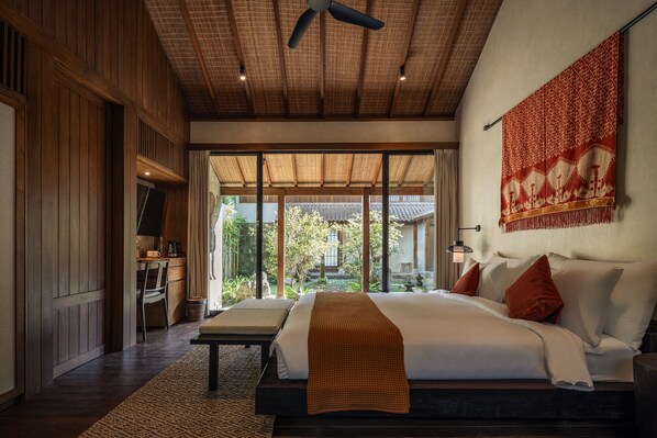 A spacious bedroom with a large bed, a ceiling fan, and a view of a traditional courtyard.